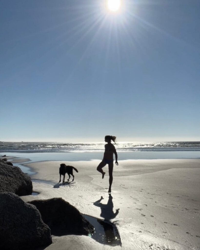 Silhouette of a woman and her dog walking on the beach in bright sunlight