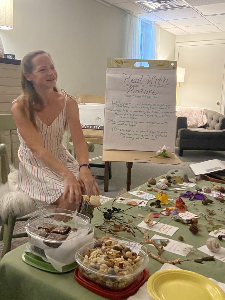 Gretchen TenBrook leading a Heal With Nature workshop beside a flip chart, with shells, stones and pressed flowers on the table