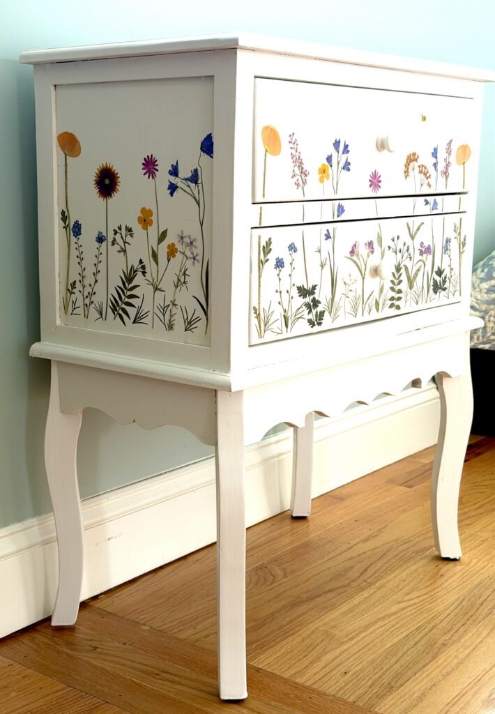 A white chest of drawers hand-decorated with pressed wildflowers and botanical stems