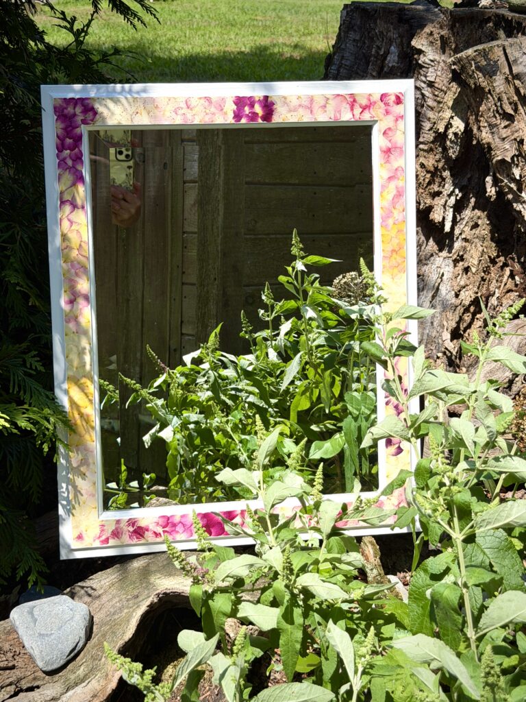 A mirror framed with pressed flowers displayed in a summer garden