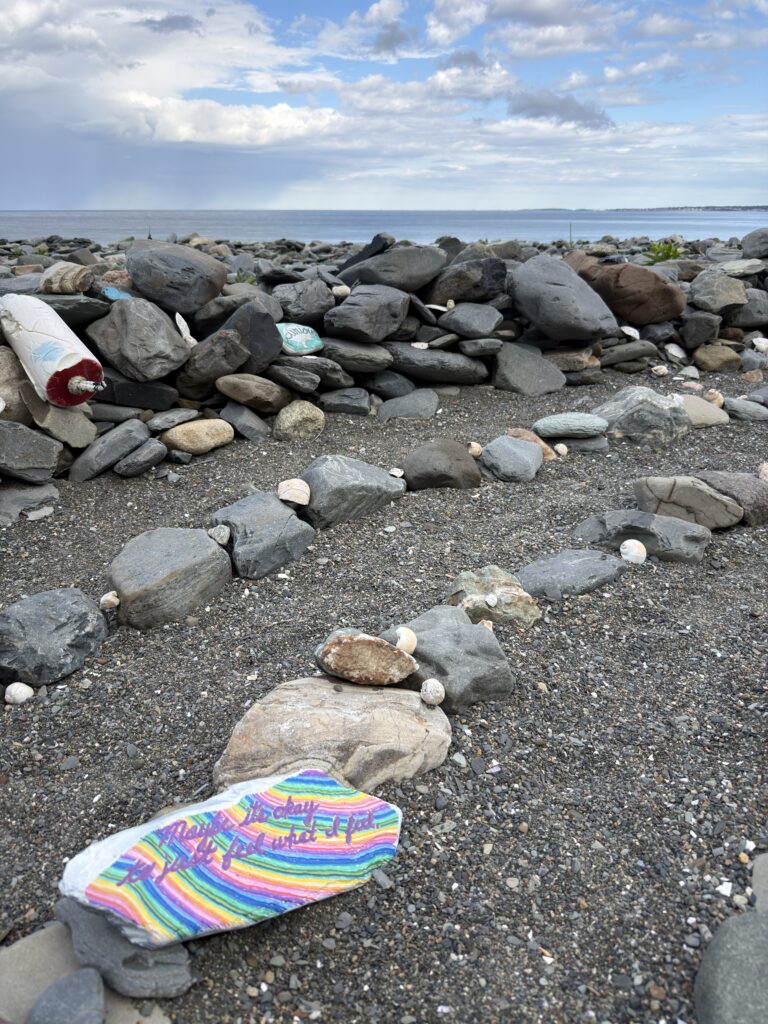 A striped hand-painted stone resting among grey beach rocks