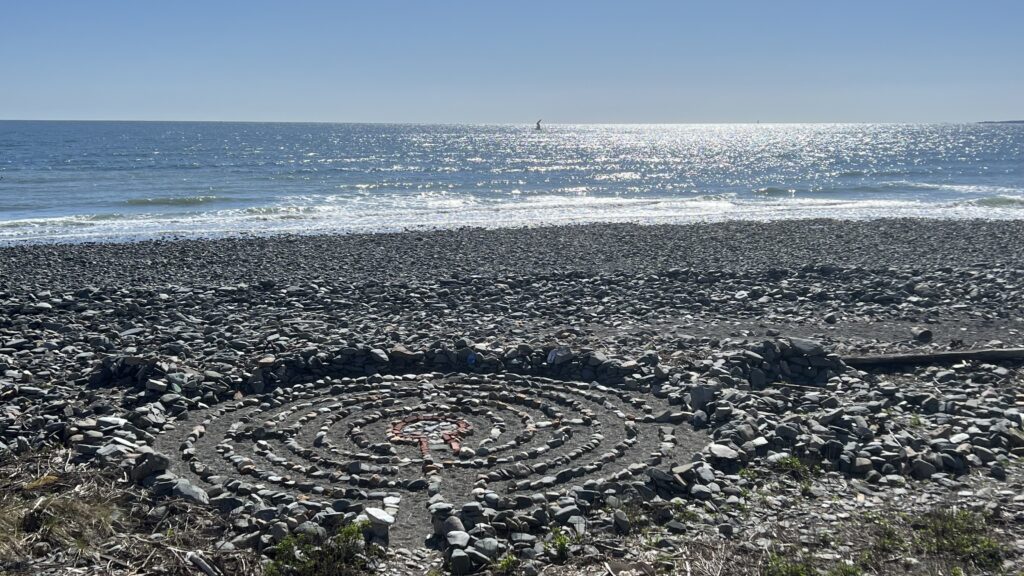 A stone labyrinth built on a pebble beach with the ocean beyond