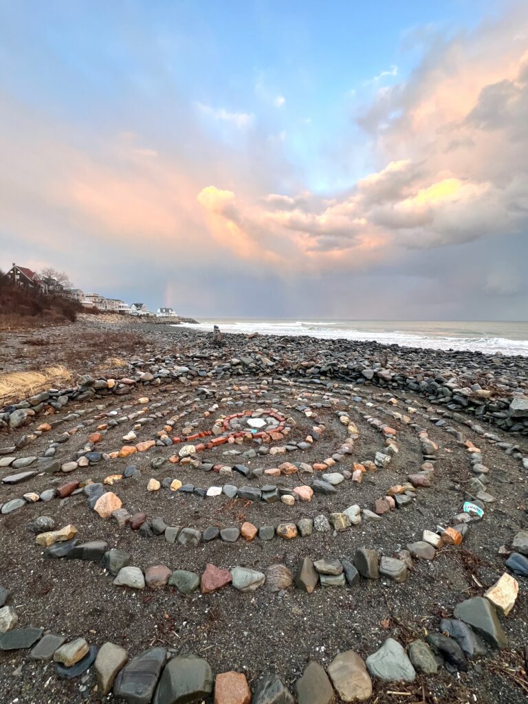 A spiral stone labyrinth on the shoreline under a pink and blue sunrise sky